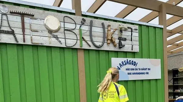 En kvinnlig medarbetare i varselkläder står framför en grön container.